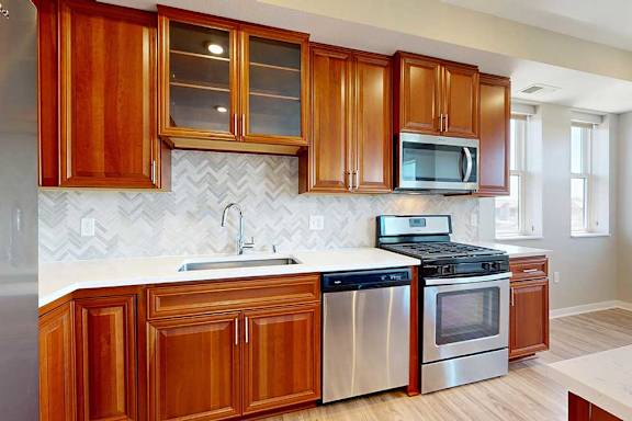 A kitchen with cherry-stained wooden cabinets, light quartz countertops, and stainless steel appliances.