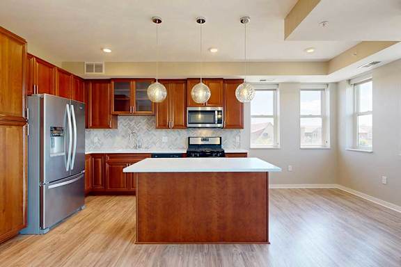 A kitchen with cherry-stained wooden cabinets, light quartz countertops, stainless steel appliances, and an island with pendant lighting.