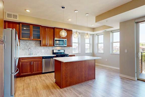 A kitchen with cherry-stained wooden cabinets, light quartz countertops, stainless steel appliances, and an island with pendant lighting.