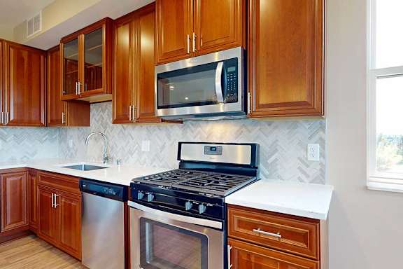 A close up of a stainless steel range and microwave in a kitchen with cherry-stained wooden cabinets.