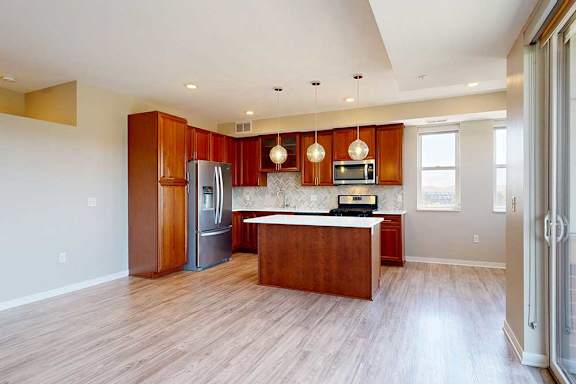 A kitchen with cherry-stained wooden cabinets, light quartz countertops, stainless steel appliances, and an island with pendant lighting.