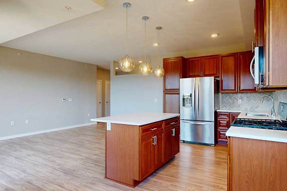 A kitchen with cherry-stained wooden cabinets, light quartz countertops, stainless steel appliances, and an island with pendant lighting.