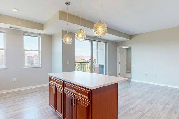 A kitchen island with cherry-stained wooden cabinets and a light quartz countertop, in front of a spacious living room.