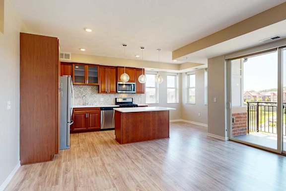 A living room with hardwood-style flooring, open to a modern kitchen with cherry-stained wooden cabinets.