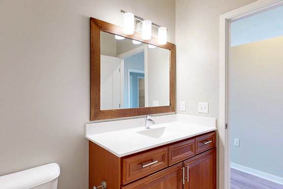 A bathroom with a white quartz vanity sink, an oversized mirror, and overhead lighting.