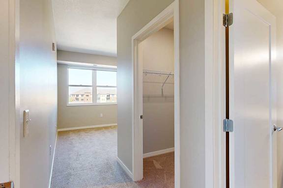 A carpeted bedroom with a large window, an attached walk-in closet, and attached bathroom.