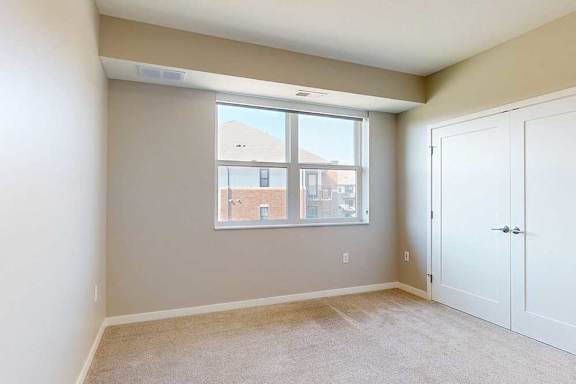 A carpeted bedroom with a large window and a double-door closet.
