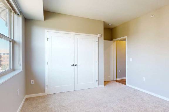 A carpeted bedroom with a large window and a double-door closet.