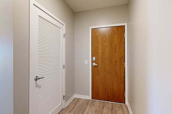 An entryway with a wooden front door and a white slatted door to a laundry room.