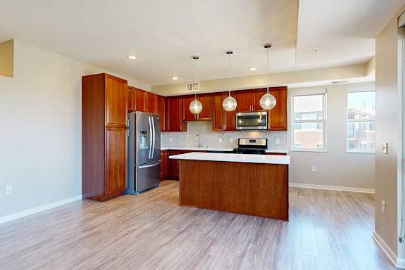 A kitchen with cherry-stained wooden cabinets, light quartz countertops, stainless steel appliances, and an island with pendant lighting.