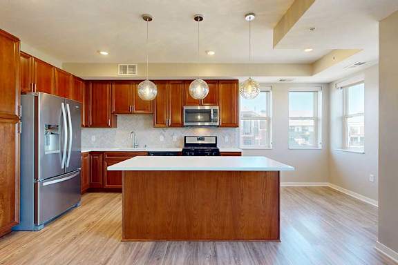 A kitchen with cherry-stained wooden cabinets, light quartz countertops, stainless steel appliances, and an island with pendant lighting.