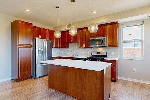 A kitchen with cherry-stained wooden cabinets, light quartz countertops, stainless steel appliances, and an island with pendant lighting.