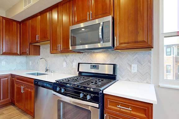 A close up of a stainless steel range and microwave in a kitchen with cherry-stained wooden cabinets.
