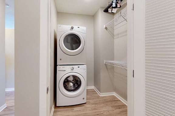 A laundry room with a stacked washer and dryer, and built-in wire shelves.