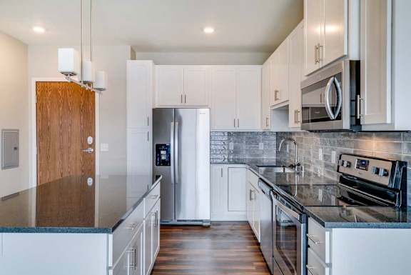 A modern kitchen with white cabinets, black granite counters, stainless steel appliances, a tile backsplash, and an island.