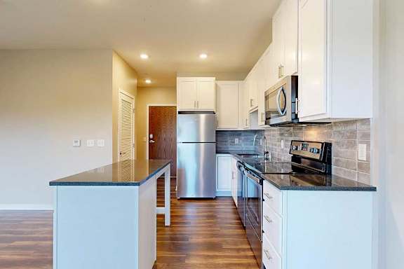 A modern kitchen with white cabinets, black granite countertops, stainless steel appliances, a tile backsplash, and an island.
