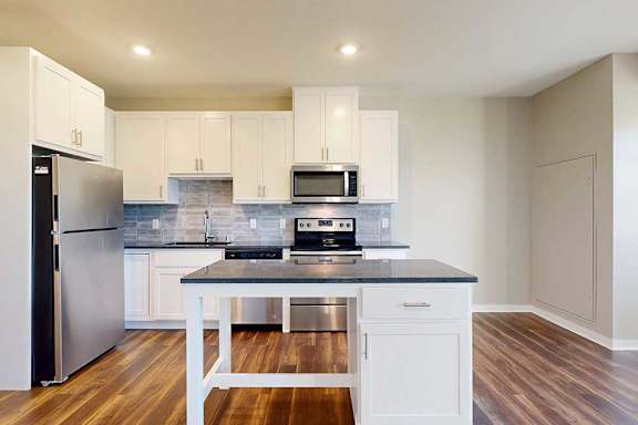 A modern kitchen with white cabinets, black granite countertops, stainless steel appliances, a tile backsplash, and an island.