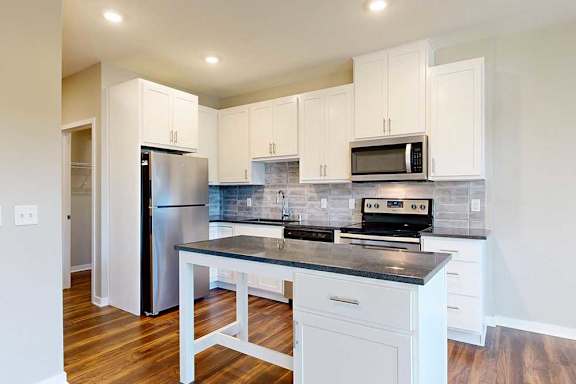 A modern kitchen with white cabinets, black granite countertops, stainless steel appliances, a tile backsplash, and an island.