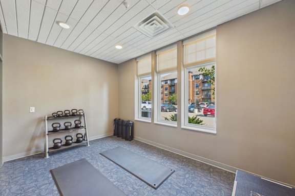 A room with a grey floor, a window with a view of a street, and a rack of kettlebells.