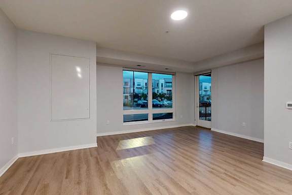 A spacious room with wooden flooring and a large window overlooking a cityscape.