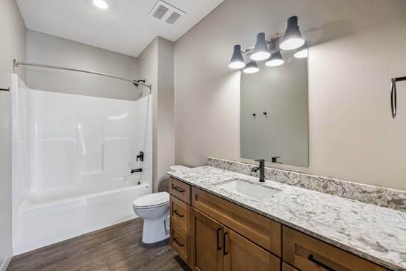 Bright apartment bathroom with a double-sink vanity, stone-look countertop, large mirror, and tub-shower combination.