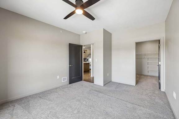 Spacious bedroom with neutral carpet, ceiling fan, and an open doorway leading toward the walk-in closet and adjoining areas.