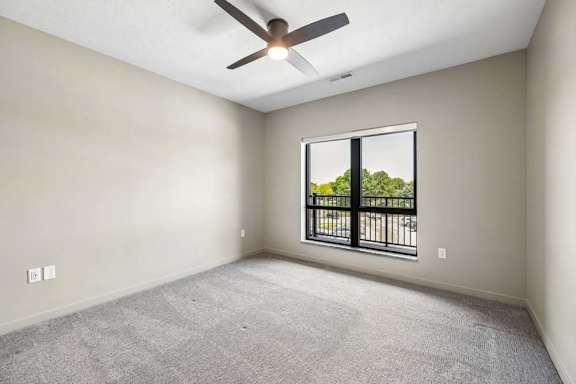 Carpeted apartment bedroom with a ceiling fan, large window for natural light, and neutral wall finishes throughout.