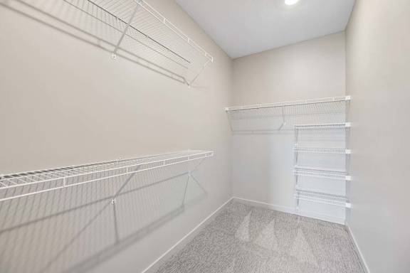 Walk-in closet with multiple wire shelving systems, carpet flooring, and ample storage space for clothing and household items.
