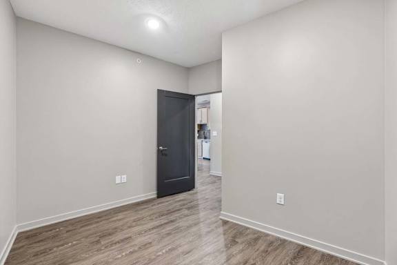 Flexible den or home office space with wood-look flooring, neutral walls, and an open layout connected to the main living area.