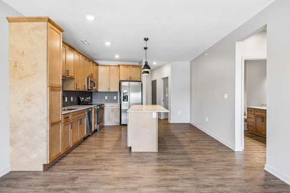 Open-concept apartment kitchen with wood cabinetry, a center island, pendant lighting, and sightlines into the living area.