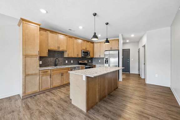 Open-concept apartment kitchen with wood cabinetry, a center island, pendant lighting, and wood-look flooring extending into the living area.