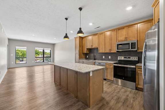Spacious kitchen and living area featuring a large island, stainless steel appliances, wood cabinets, and abundant natural light from oversized windows.