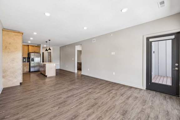 Bright open living room with wood-look flooring, recessed lighting, and a glass door leading to the private balcony.