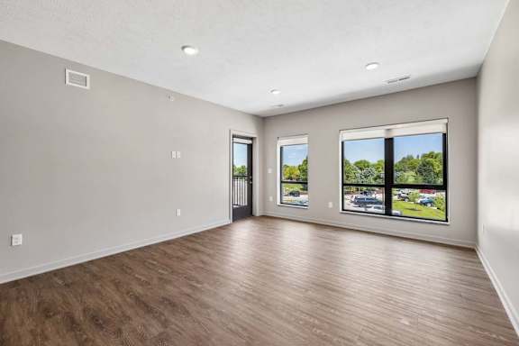 Spacious apartment living room with large windows, wood-look flooring, and views of the surrounding community.