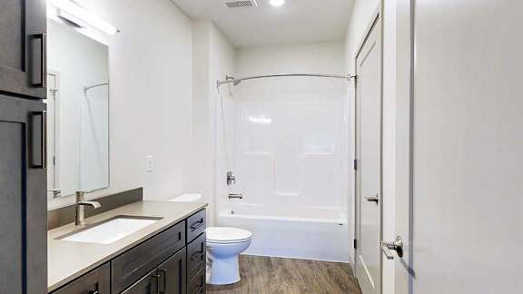 a bathroom with a dark wood vanity sink, quartz countertops, and a white tub shower