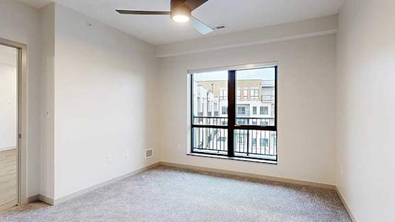 a bedroom with a large window looking out to the balcony and a ceiling fan