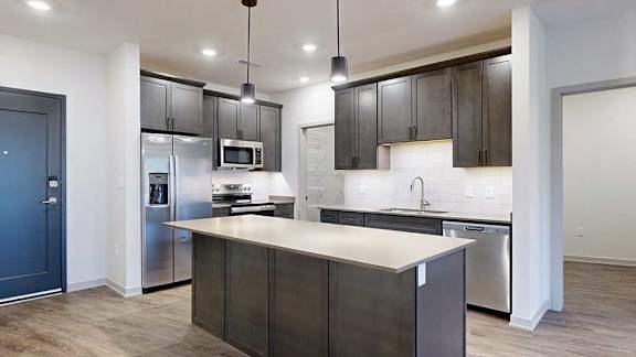 a modern kitchen with dark wood cabinets, quartz countertops, stainless steel appliances, and a large central island