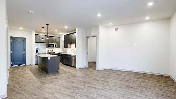 an open-concept living room and kitchen with hardwood flooring, dark wooden cabinets, and quartz countertops