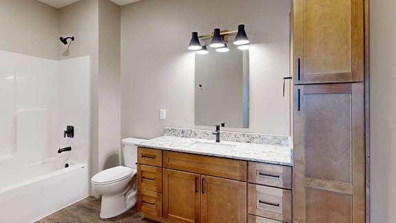 a bathroom with a light brown cabinets, a tall storage cabinet, quartz vanity sink, a mirror, and a shower and tub