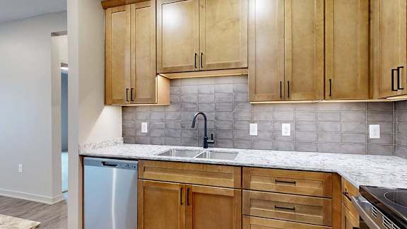 a kitchen with light brown cabinets, quartz countertops, and a tile backsplash