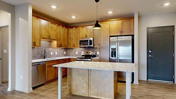 a kitchen with a large table island, light brown wooden cabinets, quartz countertops, and stainless steel appliances