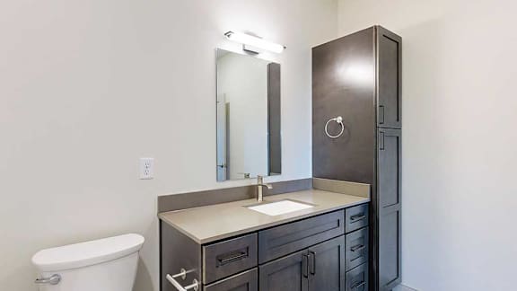 a bathroom with a quartz vanity sink, a tall dark wooden storage cabinet, and a mirror with overhead lighting