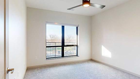 a bedroom with carpeted flooring, a ceiling fan, and a large window looking out to a balcony