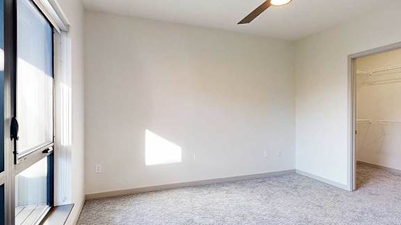 a bedroom with carpeted flooring, a ceiling fan, a large window, and a walk-in closet