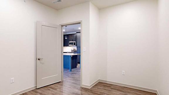 a den space with hardwood flooring, white walls, and a door to the kitchen