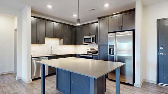 a modern kitchen with dark wood cabinets, light quartz countertops, a tile backsplash, a large central island, and stainless steel appliances