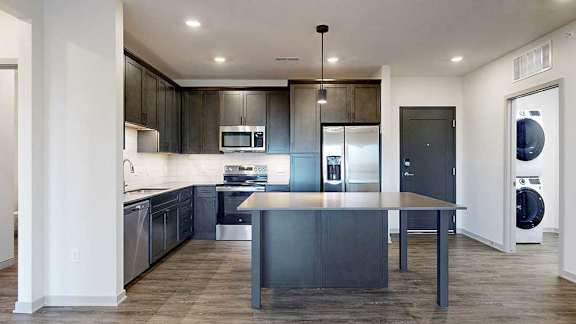 a modern kitchen with dark wood cabinets, light quartz countertops, a tile backsplash, a large central island, and stainless steel appliances