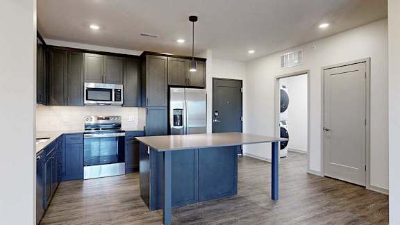 a modern kitchen with dark wood cabinets and a central island next to a front door and laundry room
