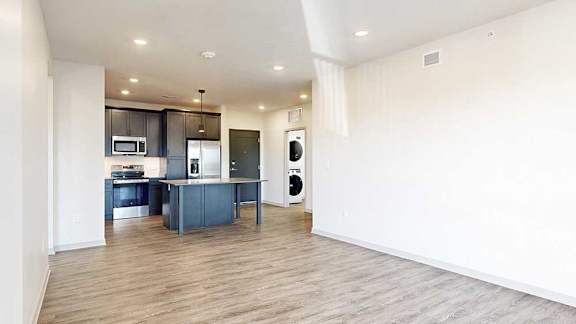 a living room with hardwood flooring next to a kitchen with dark cabinets and a large central island