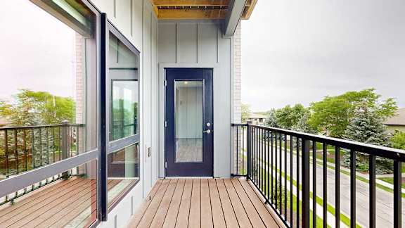 A balcony with a metal railing, a windowed door to the living room, and a view of the neighborhood.